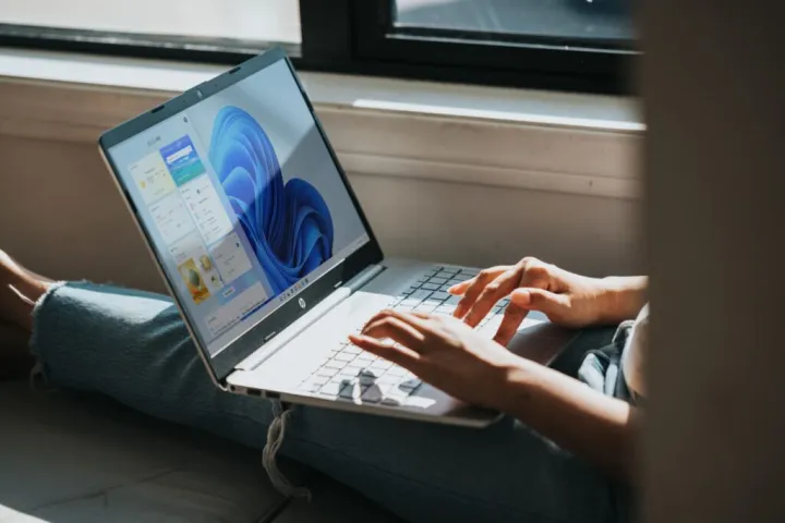 شخص يستخدم جهاز كمبيوتر محمول يعمل بنظام Windows 11 على حجره بجانب النافذة.