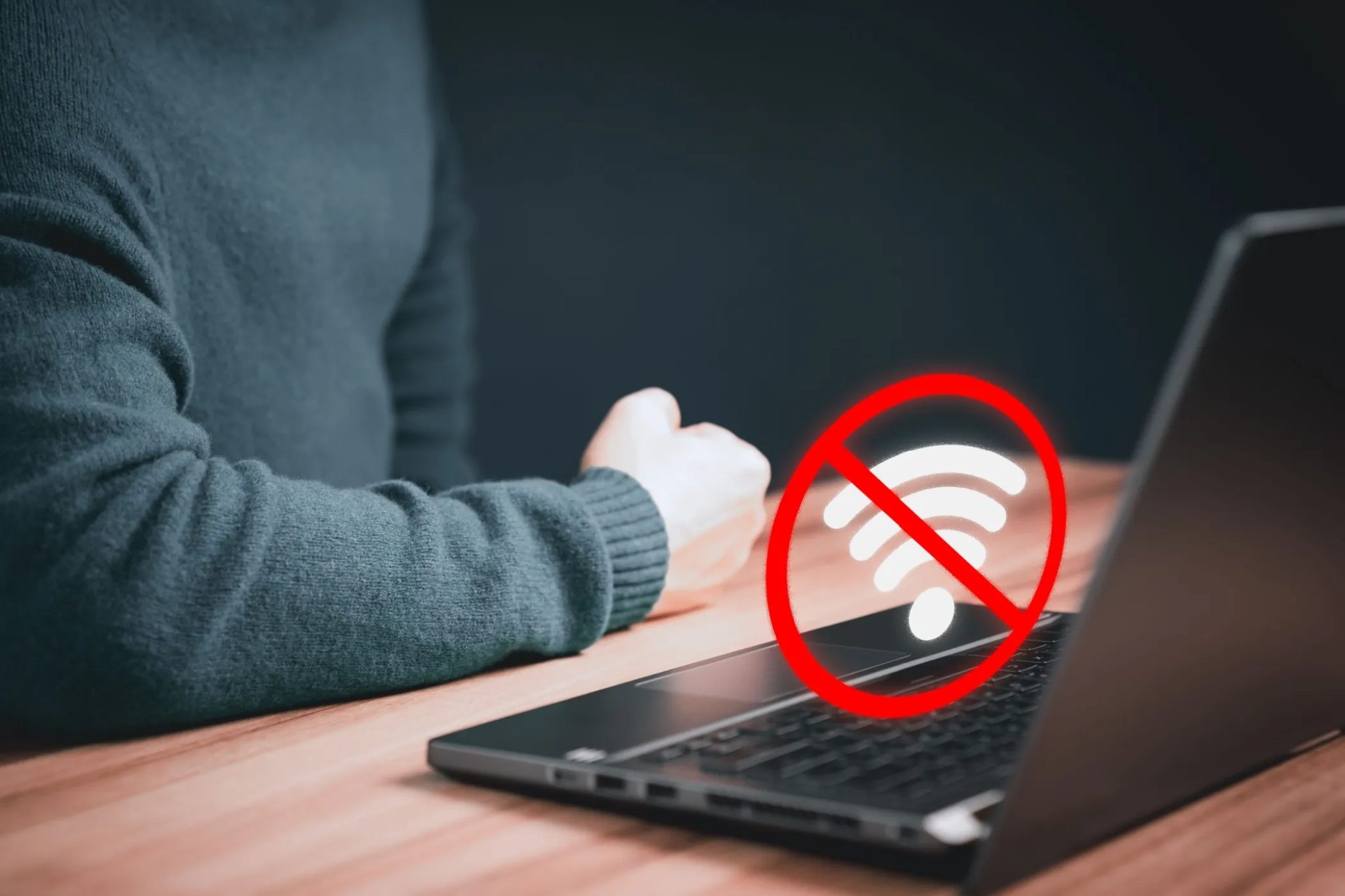 رمز انقطاع اتصال Wi-Fi فوق جهاز كمبيوتر محمول مع ذراع شخص على الطاولة