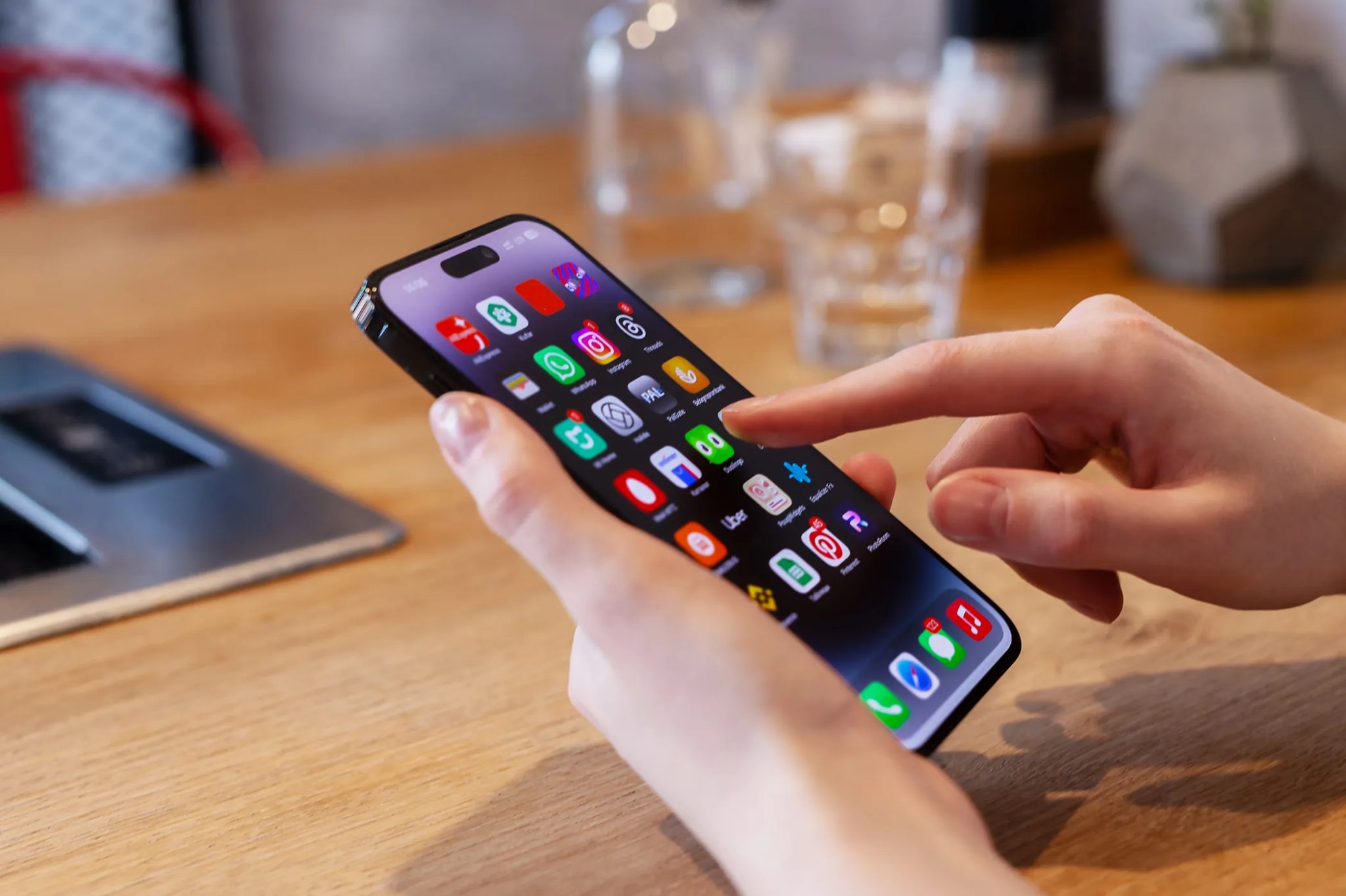شخص يستخدم iPhone على طاولة مع وجود كوب زجاجي خلفه.