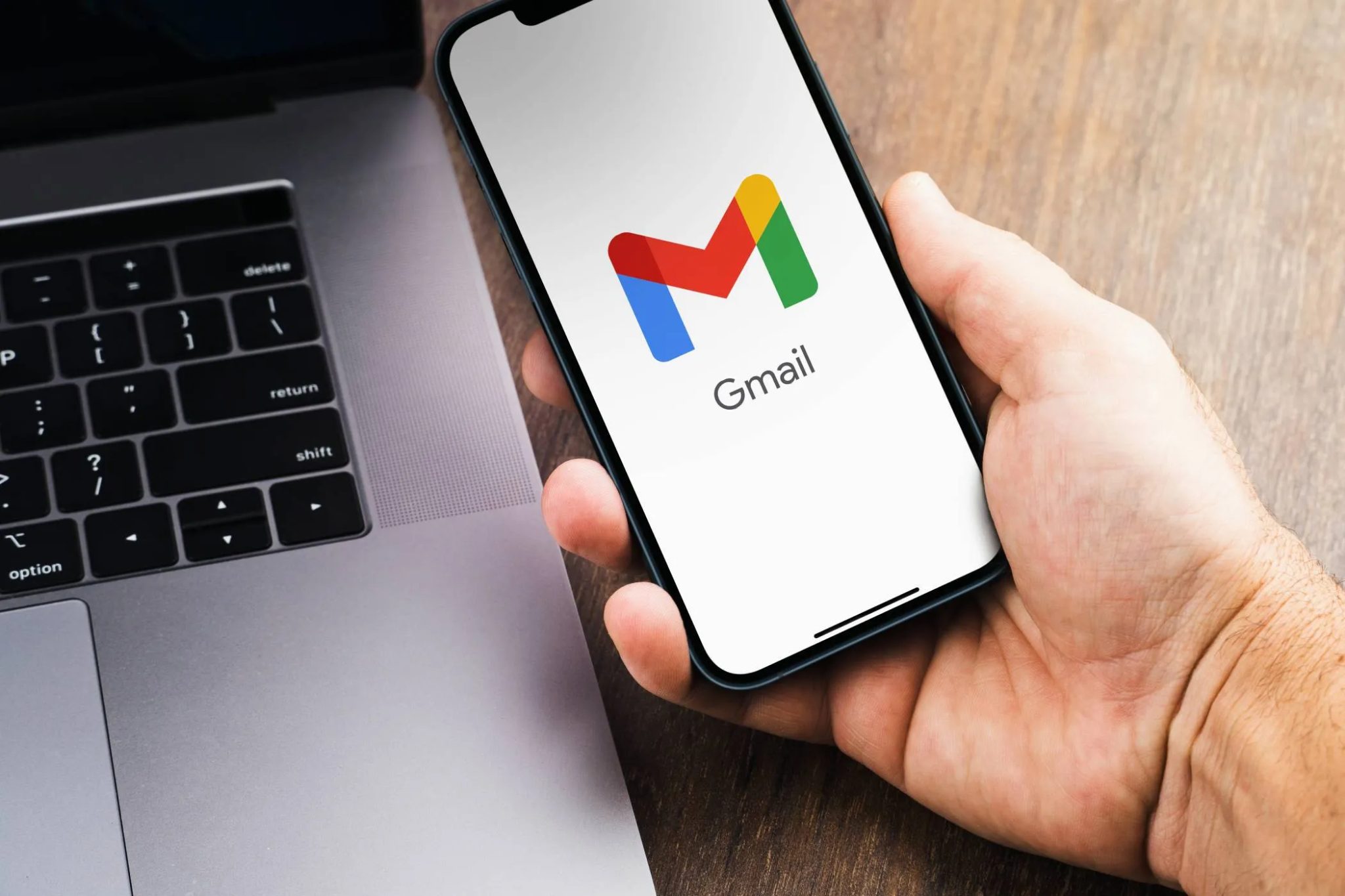 شعار Gmail يظهر على شاشة هاتف ذكي بجوار جهاز كمبيوتر محمول